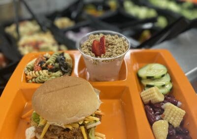 A lunch trya containing pulled pork sandwich, salad and yogurt cup.