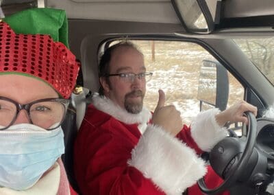 Two people, one dressed as santa and driving and another with an elf hat on.
